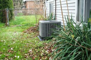 Outdoor AC unit next to a house surrounded by plants, potential candidate for AC repair or replacement service.